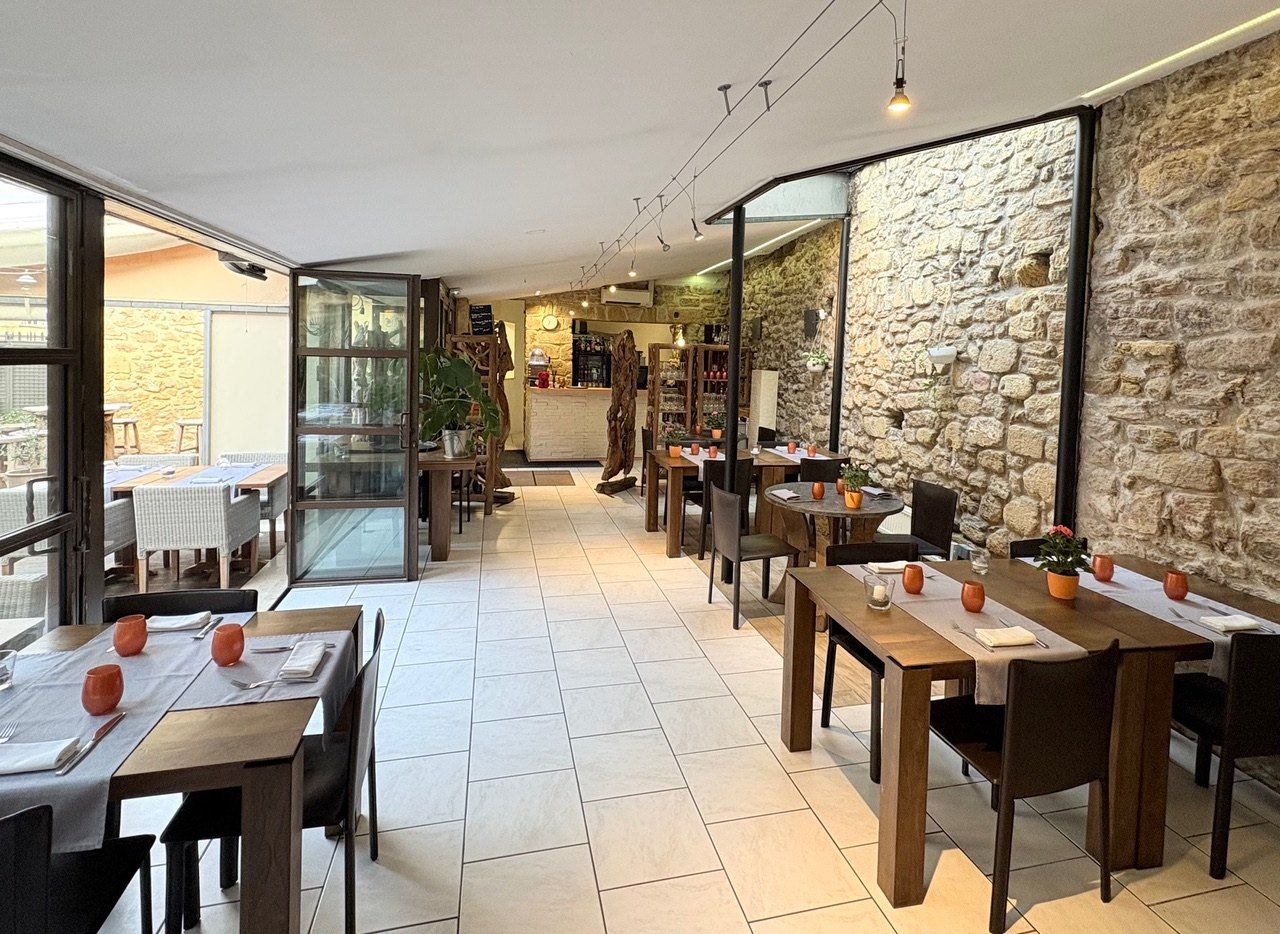 La salle aux murs de pierre, ses tables dressées et la verrière sur la terrasse